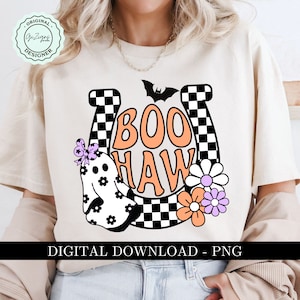 May include: Cream-colored t-shirt with a Halloween-themed graphic. The design features the words "BOO HAW" in orange, a ghost, flowers, and a bat. The design is set against a horseshoe shape with a checkered pattern. The text "DIGITAL DOWNLOAD - PNG" is at the bottom.