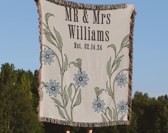 May include: A woven throw blanket with a cream background and a floral design in shades of green and blue. The text "MR & Mrs Williams Est. 02.14.24" is printed in black.