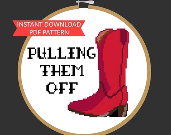 May include: A white embroidery hoop with a red cowboy boot and the text "PULLING THEM OFF" in black. The hoop is on a dark grey background.