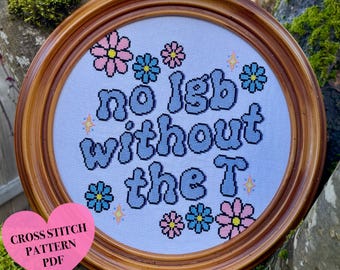 May include: Circular, framed cross-stitch artwork featuring the phrase "no lgb without the T" in blue bubble lettering. The design incorporates pink, blue, and yellow floral and star motifs. The frame is a light brown hue. A pink heart-shaped tag reads "Cross Stitch Pattern PDF."