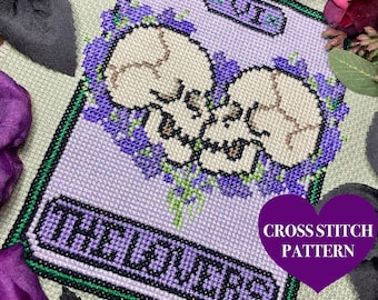 May include: Cross stitch pattern for a tarot card, The Lovers, featuring two white skulls with purple flowers. The card is labelled with the Roman numeral VI and the word "Lovers".