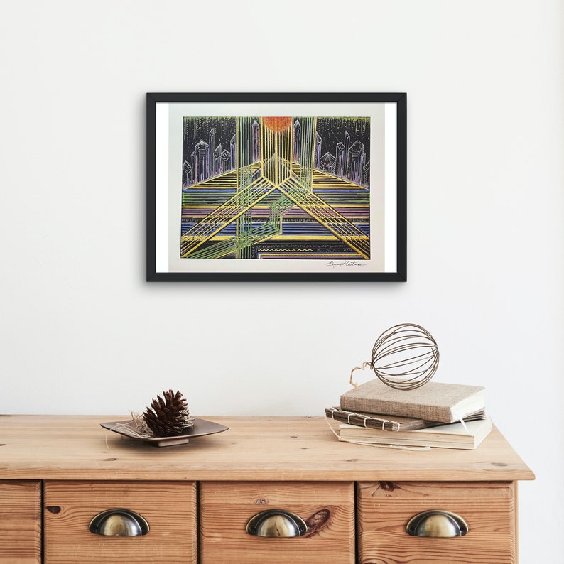May include: A framed abstract art print with a black frame. The print features a colorful cityscape with a yellow, orange, and red sun in the center. The cityscape is made up of lines and shapes in shades of blue, green, and purple.