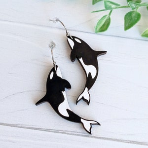 May include: A pair of silver earrings with black and white orca whale charms. The whales are facing opposite directions and have a white underbelly.