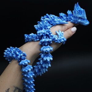 May include: A long, articulated dragon figurine featuring a vibrant blue and white marbled finish. The creature has a segmented, flexible body with intricate scale-like textures and a detailed head, designed to drape and coil around an object.