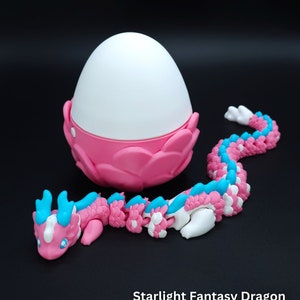 May include: A pink and blue segmented dragon toy with a white egg-shaped head. The dragon is curled up around the egg, which is also pink and has white accents. The text "Starlight Fantasy Dragon" is printed below the toy.
