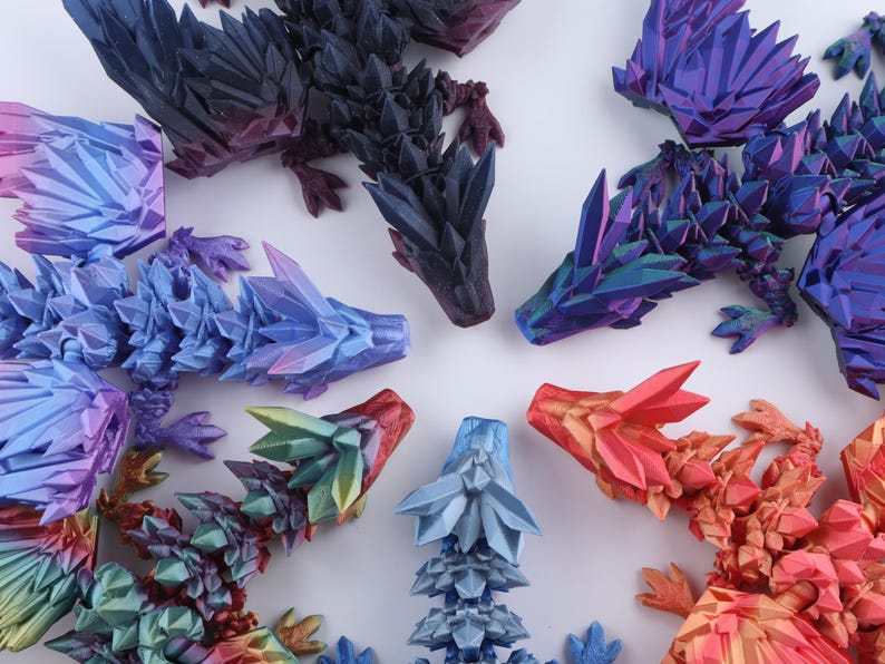 Puede incluir: Una colecci&oacute;n de cinco figuras de drag&oacute;n articuladas con una textura facetada similar al cristal. Los dragones est&aacute;n coloreados en degradados de morado oscuro, azul y morado iridiscente, azul claro, verde y amarillo, y naranja y rojo.