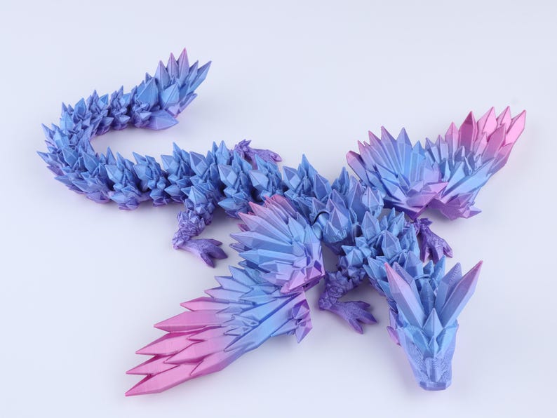 Puede incluir: Una figura de drag&oacute;n articulada con una textura geom&eacute;trica cristalina. El cuerpo presenta un degradado de color azul profundo a magenta vibrante, con p&uacute;as angulares afiladas que cubren la cabeza, las alas, el lomo y la larga cola curvada.