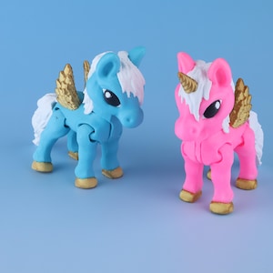 May include: Two small plastic figurines of winged horses. One is light blue with a white mane and tail, gold wings, and gold hooves. The other is bright pink with a white mane and tail, a gold horn, gold wings, and gold hooves. Both have large black eyes.