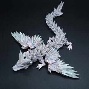 Puede incluir: Una figura de drag&oacute;n articulada de color blanco con una textura geom&eacute;trica compleja similar a un cristal que cubre todo el cuerpo, incluidas las alas y la larga cola segmentada. La superficie tiene sutiles reflejos iridiscentes y bordes afilados.