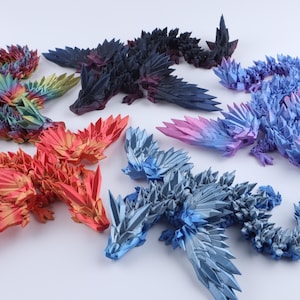 Puede incluir: Una colecci&oacute;n de seis figuras de drag&oacute;n articuladas con escamas geom&eacute;tricas afiladas que parecen cristales. Los dragones se muestran en varios colores, incluyendo un degradado de arco&iacute;ris, rojo s&oacute;lido, negro profundo, azul claro y un degradado de azul a morado.