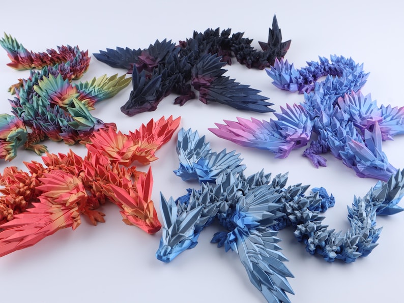 Puede incluir: Una colecci&oacute;n de seis figuras de drag&oacute;n articuladas con escamas geom&eacute;tricas afiladas que parecen cristales. Los dragones se muestran en varios colores, incluyendo un degradado de arco&iacute;ris, rojo s&oacute;lido, negro profundo, azul claro y un degradado de azul a morado.