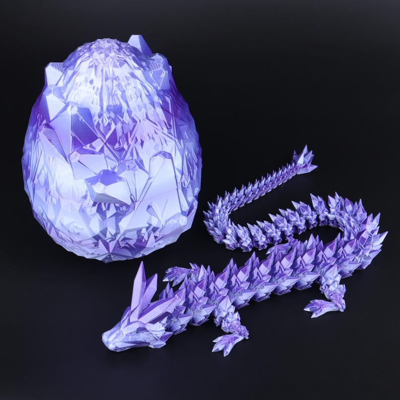 May include: A purple, crystalline dragon figurine with a matching egg and tail. The dragon is in a lying position, with sharp, angular details. The egg is large and textured, and the tail is curved. The objects are on a black surface.