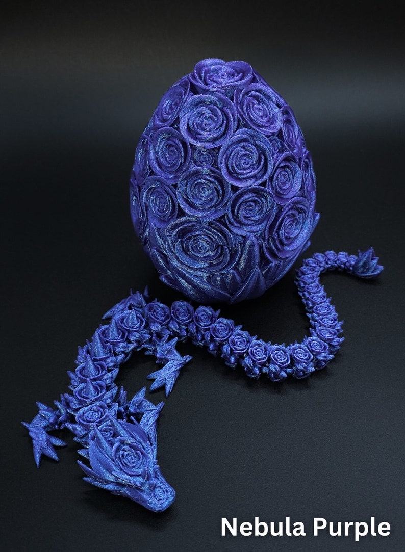 May include: A 3D printed purple dragon figure with a body composed of rose-like textures, positioned next to an egg covered in similar rose patterns. The object is labeled Nebula Purple. The dragon has a long, segmented body and a detailed head.