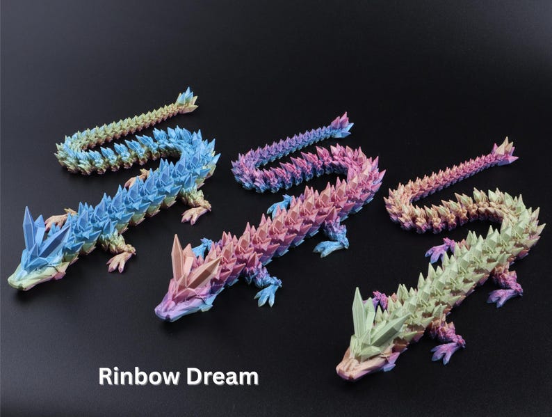 May include: Five colorful dragon figurines in shades of blue, pink, purple, and green. Each dragon has a spiky, crystal-like design and is posed on a dark surface. The text "Rainbow Dream" is at the bottom.