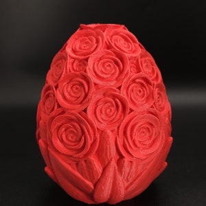 May include: A bright red, egg-shaped object featuring a textured surface covered in numerous sculpted rose patterns. The design consists of multiple layered floral shapes that wrap around the entire exterior of the oval form, creating a dense, uniform, and repeating botanical relief pattern across the surface.