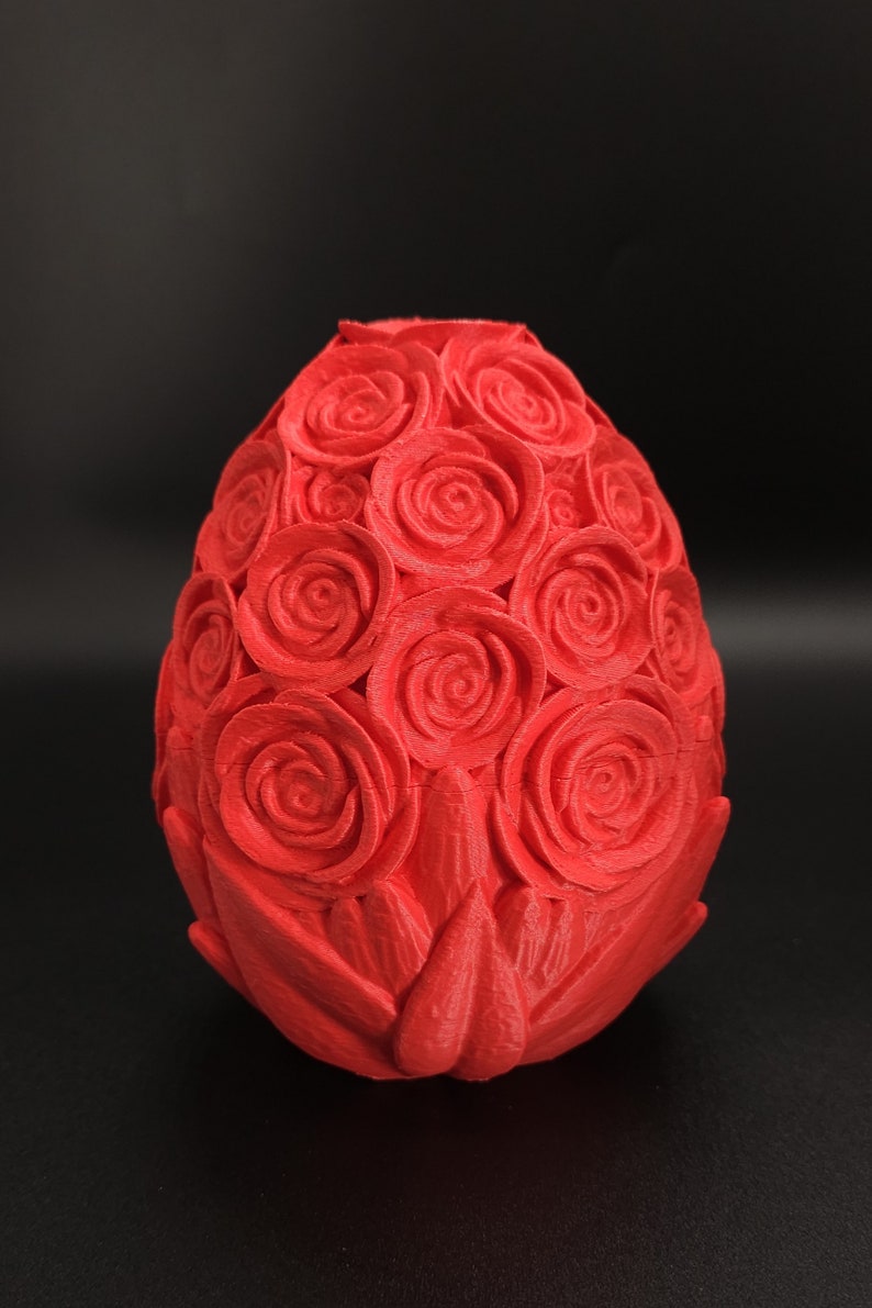 May include: A bright red, egg-shaped object featuring a textured surface covered in numerous sculpted rose patterns. The design consists of multiple layered floral shapes that wrap around the entire exterior of the oval form, creating a dense, uniform, and repeating botanical relief pattern across the surface.