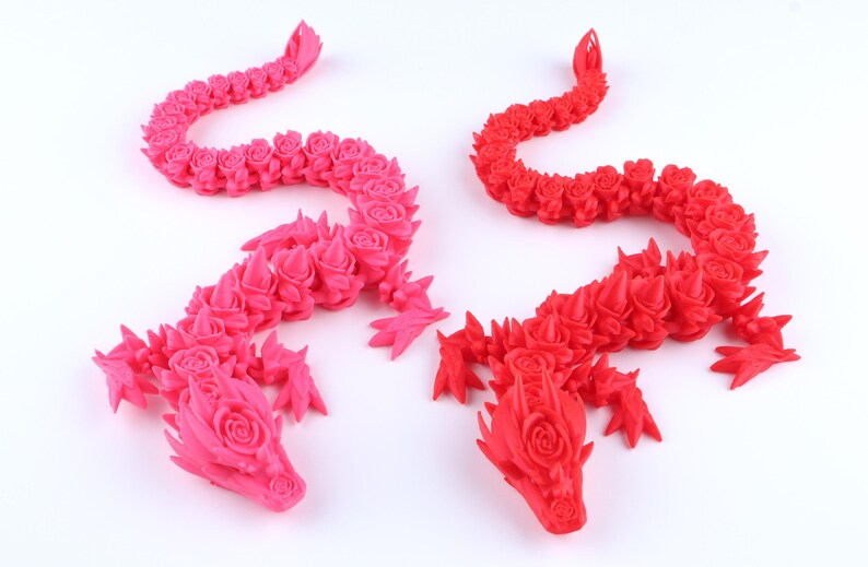 May include: Two articulated dragon figurines, one in bright pink and one in vibrant red. Each dragon features a detailed, segmented body composed of repeating rose-like floral patterns, with sharp, pointed spikes along the back and head.