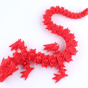 May include: A bright red articulated dragon figurine constructed from a series of interconnected rose-shaped segments. The creature features a detailed head with rose-like textures, four pointed limbs, and a long, winding tail composed of individual roses.