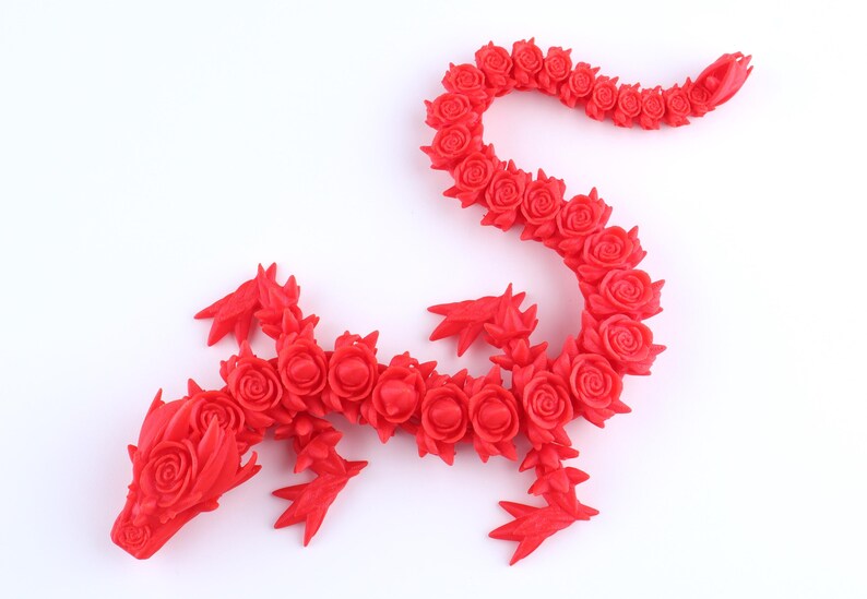 May include: A bright red articulated dragon figurine constructed from a series of interconnected rose-shaped segments. The creature features a detailed head with rose-like textures, four pointed limbs, and a long, winding tail composed of individual roses.