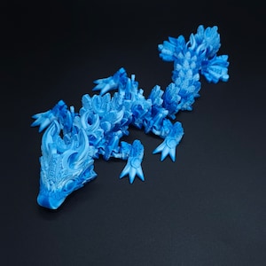 May include: A bright blue articulated lizard figurine featuring a complex, layered scale pattern across its body, head, and tail. The creature has four legs with pointed claws and a detailed, textured surface design throughout its entire form.