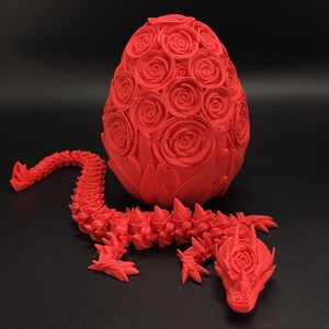 May include: A bright red 3D printed articulated dragon figure with a rose-textured body, positioned next to a matching egg-shaped container covered in a detailed pattern of sculpted roses, both featuring a matte finish and intricate floral details.