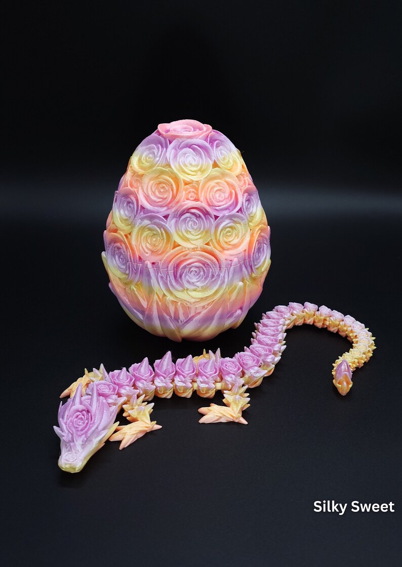May include: An oval egg covered in a relief pattern of roses and a long, articulated dragon figure, both featuring a gradient color scheme of pastel pink, yellow, and purple. The text Silky Sweet is printed in the bottom right corner.