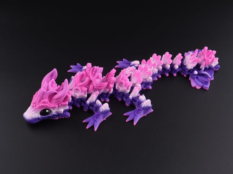 May include: An articulated dragon figurine featuring a gradient color scheme that transitions from deep purple at the base to bright pink and white along the dorsal ridges. The creature has large black eyes and a segmented body with four legs.