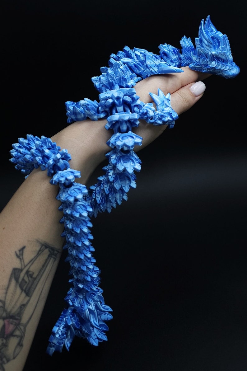 May include: A long, articulated dragon figurine featuring a vibrant blue and white marbled finish. The creature has a segmented, flexible body with intricate scale-like textures and a detailed head, designed to drape and coil around an object.