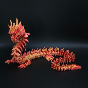 May include: A red and gold shiny dragon figurine with a long, segmented tail. The dragon has a detailed head with sharp teeth and horns.