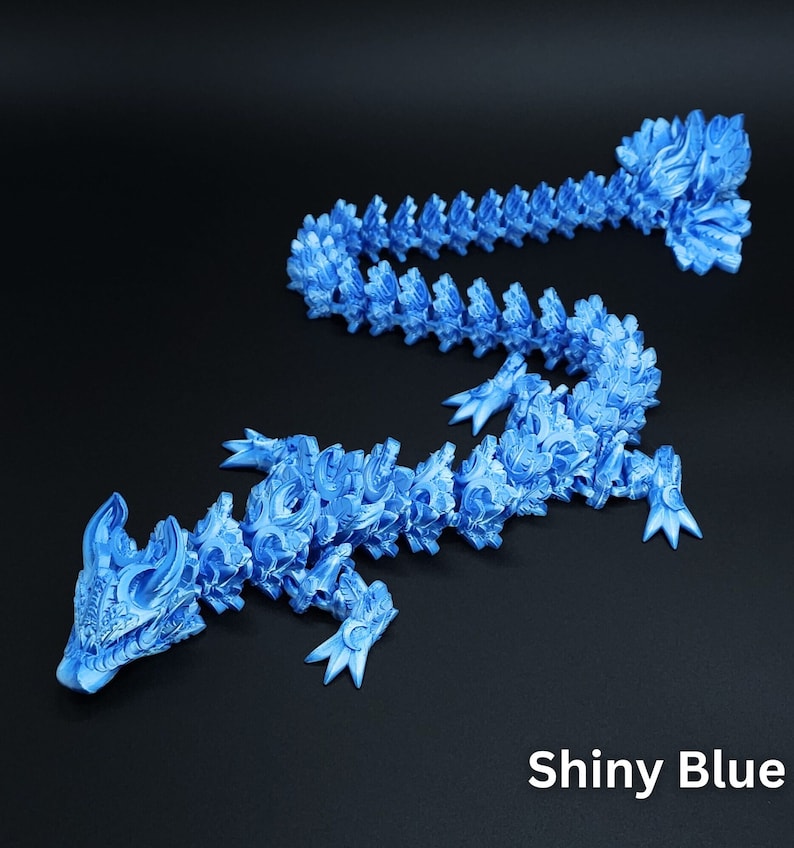 May include: A shiny blue articulated dragon figurine with a segmented, flexible body and intricate scale-like detailing. The creature features a horned head, four clawed limbs, and a long, winding tail. The text "Shiny Blue" is visible.