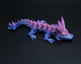 Può includere: Una statuetta di lucertola stampata in 3D con un gradiente di colore rosa e blu. La lucertola ha una schiena spinosa e un muso lungo.