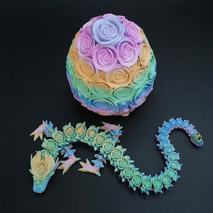 May include: A 3D printed articulated dragon figure and a matching egg, both covered in a textured rose pattern. The dragon and egg feature a gradient color scheme transitioning through shades of pastel pink, blue, yellow, and green.