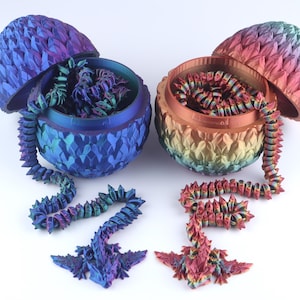 May include: Two articulated dragon figures emerging from matching scale-textured eggs. One dragon and egg set features a blue and purple gradient, while the other displays a warm red, orange, and yellow gradient. Both figures have long, segmented bodies.