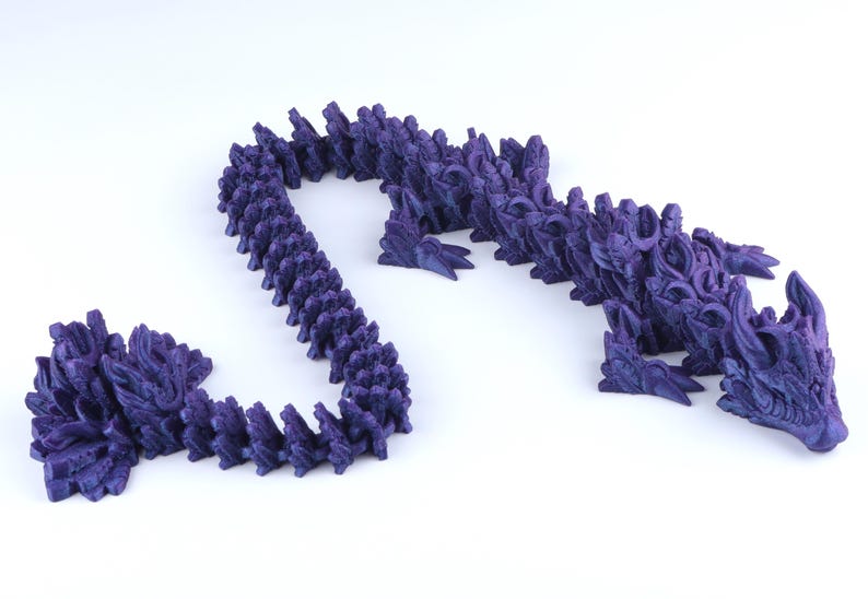 May include: A dark purple articulated dragon figurine featuring a segmented body with intricate scale textures, a detailed head with horns, and four limbs. The flexible design allows the creature to curve into various positions on a plain surface.