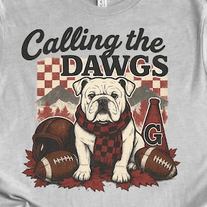 Puede incluir: Camiseta gris claro con un diseño de bulldog, balones de fútbol americano y el texto "Calling the Dawgs". La camiseta tiene un diseño vintage con temática de fútbol americano. También se muestran las palabras "Bulldogs Vintage PNG".