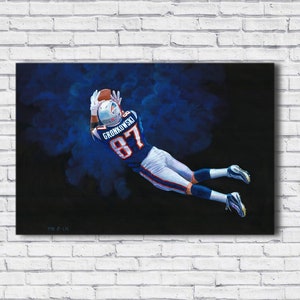 May include: A painting of a football player in a blue and white uniform, catching a football. The player is mid-air, reaching for the ball with outstretched arms. The jersey number 87 is visible. The background is dark with blue accents.