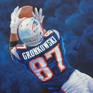 May include: Painting of an American football player in a blue and white uniform, catching a brown football. The player's jersey has the number 87 and the name GRONKOWSKI. The background is a dark blue, smoky effect.