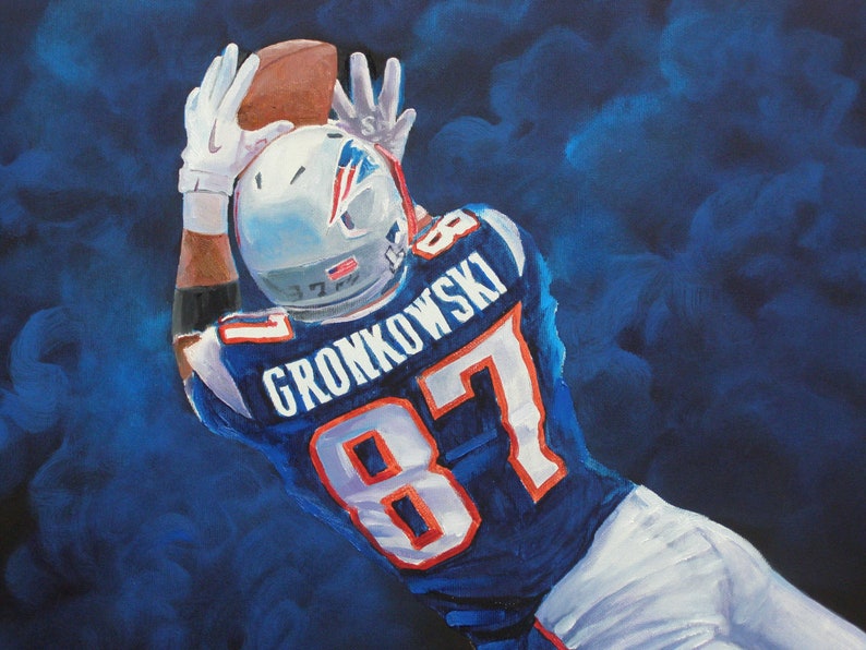 May include: Painting of an American football player in a blue and white uniform, catching a brown football. The player's jersey has the number 87 and the name GRONKOWSKI. The background is a dark blue, smoky effect.