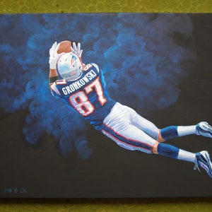 May include: An oil painting of a football player in a blue and white uniform, catching a brown football. The player is mid-air against a dark background with blue smoke effects. The jersey reads "GRONKOWSKI 87".
