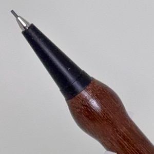 May include: Close-up of a mechanical pencil with a dark brown wooden barrel and a black tip. The pencil's metal tip is silver, and the lead is visible. The wooden barrel has a smooth, polished finish.