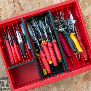 Peut inclure: Un plateau organisateur d'outils en plastique rouge avec des séparateurs noirs contenant divers outils à main, notamment des pinces, des cisailles, un cutter, des marqueurs et une clé à molette. Les outils ont des manches rouges, jaunes et noirs.