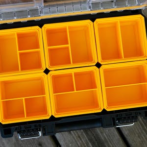 May include: A black plastic storage organizer case featuring a clear lid and six removable bright yellow interior bins. Each yellow bin is divided into smaller compartments of varying sizes to provide organized storage for small hardware items.