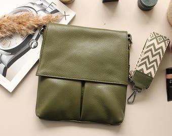 May include: Olive green leather crossbody bag with a flap closure and a patterned strap. The bag has a textured appearance and a silver-tone clasp. A magazine and other accessories are in the background.