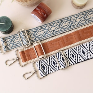 Puede incluir: Tres correas decorativas para bolsos con patrones geométricos azules y blancos, marrones y negros y blancos. Cada correa tiene herrajes metálicos plateados y un clip. También hay velas y un pequeño libro en la imagen.