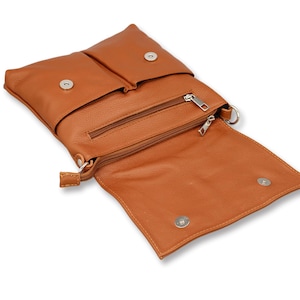 Peut inclure: Un sac bandouli&egrave;re en cuir marron clair avec un rabat et deux fermetures &agrave; bouton-pression. Le sac poss&egrave;de une poche zipp&eacute;e et une petite sangle. Le sac est ouvert, r&eacute;v&eacute;lant l'int&eacute;rieur.
