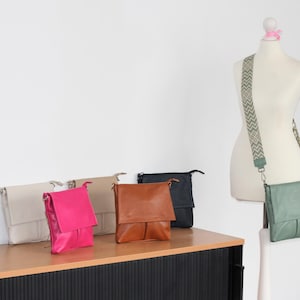 Peut inclure: Plusieurs sacs &agrave; bandouli&egrave;re en cuir de diff&eacute;rentes couleurs, dont noir, cr&egrave;me, rose vif, beige, marron et marine. Un sac est pr&eacute;sent&eacute; sur un mannequin avec une bandouli&egrave;re &agrave; motifs. Les sacs ont une fermeture &agrave; rabat et des bretelles r&eacute;glables.
