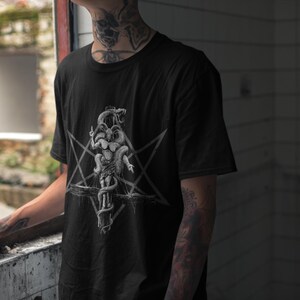 May include: Black t-shirt featuring a white graphic print of a pentagram and a creature with multiple heads.