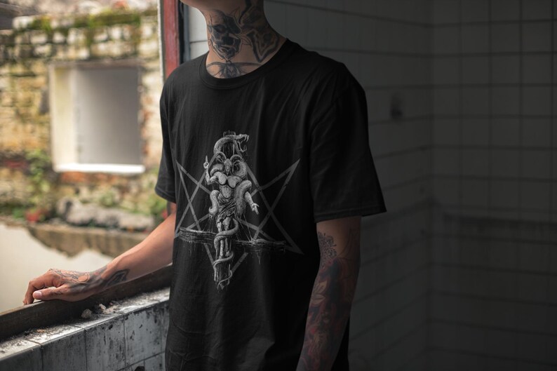 May include: Black t-shirt featuring a white graphic print of a pentagram and a creature with multiple heads.
