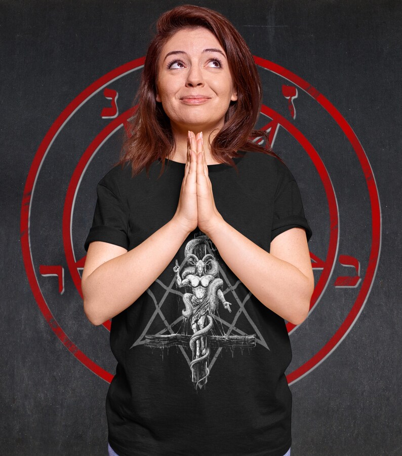 May include: A black t-shirt featuring a white graphic print of a goat-like figure with horns and a snake wrapped around it. The figure is standing on a cross with a pentagram behind it.