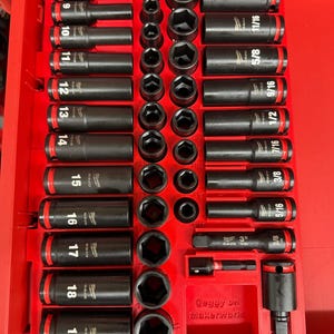 Op de afbeelding: Een rode gereedschapskist gevuld met een set zwarte slagsleutels en accessoires. De sockets zijn gelabeld met maten variërend van 9,5 mm tot 19 mm. De set bevat verschillende socketmaten en verlengstukken.